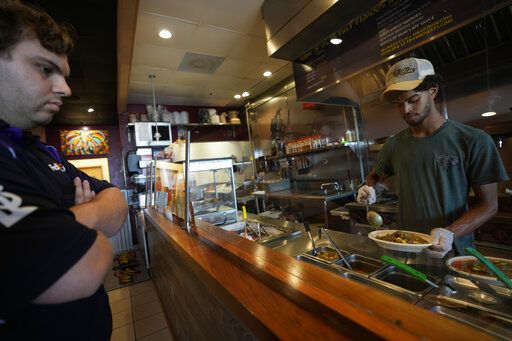Keval Bodasing, 17, prepares an order for customer Adrian Lopez, as he helps out his father, Anesh Bodasing, at his fast-casual Indian restaurant, Tiffin Box, Thursday, April 14, 2022, in West Palm Beach, Fla. The high school senior regularly volunteers to help out his dad, after the restaurant's staff dwindled to three amid a labor shortage.