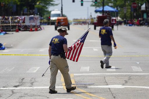 A member of the FBI's evidence response team removes an American flag one day after a mass shooting in downtown Highland Park, Ill., Tuesday, July 5, 2022. A shooter fired on an Independence Day parade from a rooftop spraying the crowd with gunshots initially mistaken for fireworks before hundreds of panicked revelers of all ages fled in terror.