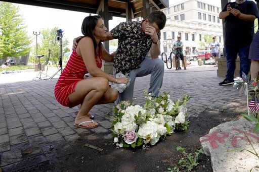 Brooke and Matt Strauss, who were married Sunday, pause after leaving their wedding bouquets in downtown Highland Park, Ill., near the scene of Monday's mass shooting Tuesday, July 5, 2022, in Highland Park, Ill.