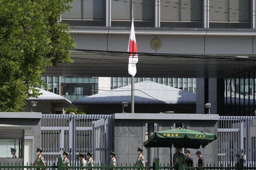Chinese paramilitary policemen march in front of the Japanese embassy where the Japanese flag is flown at half staff to commemorate the death of former Japanese Prime Minister Shinzo Abe, Saturday, July 9, 2022, in Beijing.