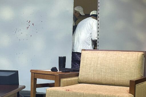Blood stains mark a screen as author Salman Rushdie, behind screen, is tended to after he was attacked during a lecture, Friday, Aug. 12, 2022, at the Chautauqua Institution in Chautauqua, N.Y., about 75 miles (120 km) south of Buffalo.